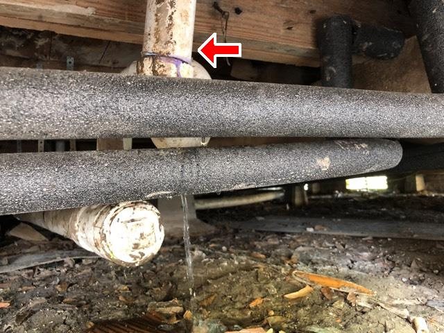 Water dripping from a drain line under the house, marked with a red arrow